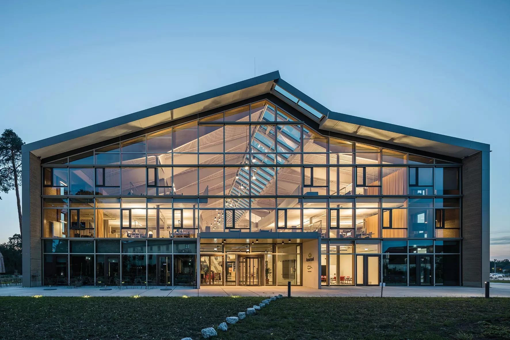 Eingang des beleuchteten Alnatura Campus von außen am Abend