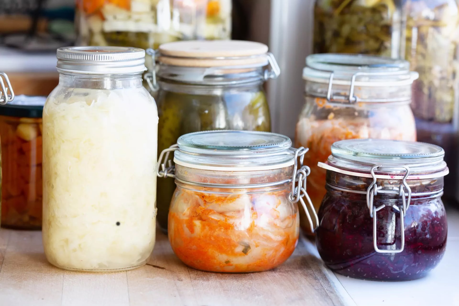 Schraubgläser gefüllt mit verschiedenen fermentierten Lebensmitteln wie Kimchi, Rotkohl und Gewürzgurken.