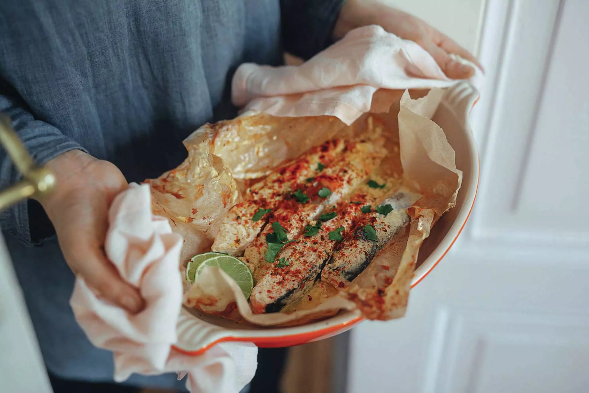 Gebackener Lachs in Joghurtmarinade in einer Auflaufform mit Backpapier. Die Auflaufform wird von zwei Händen gehalten.