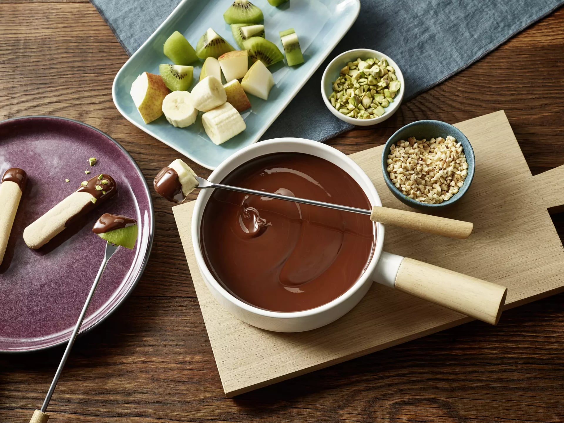 Fonduetopf mit veganem Schokoladenfondue. Daneben Schalen mit Nüssen und Obststücken.
