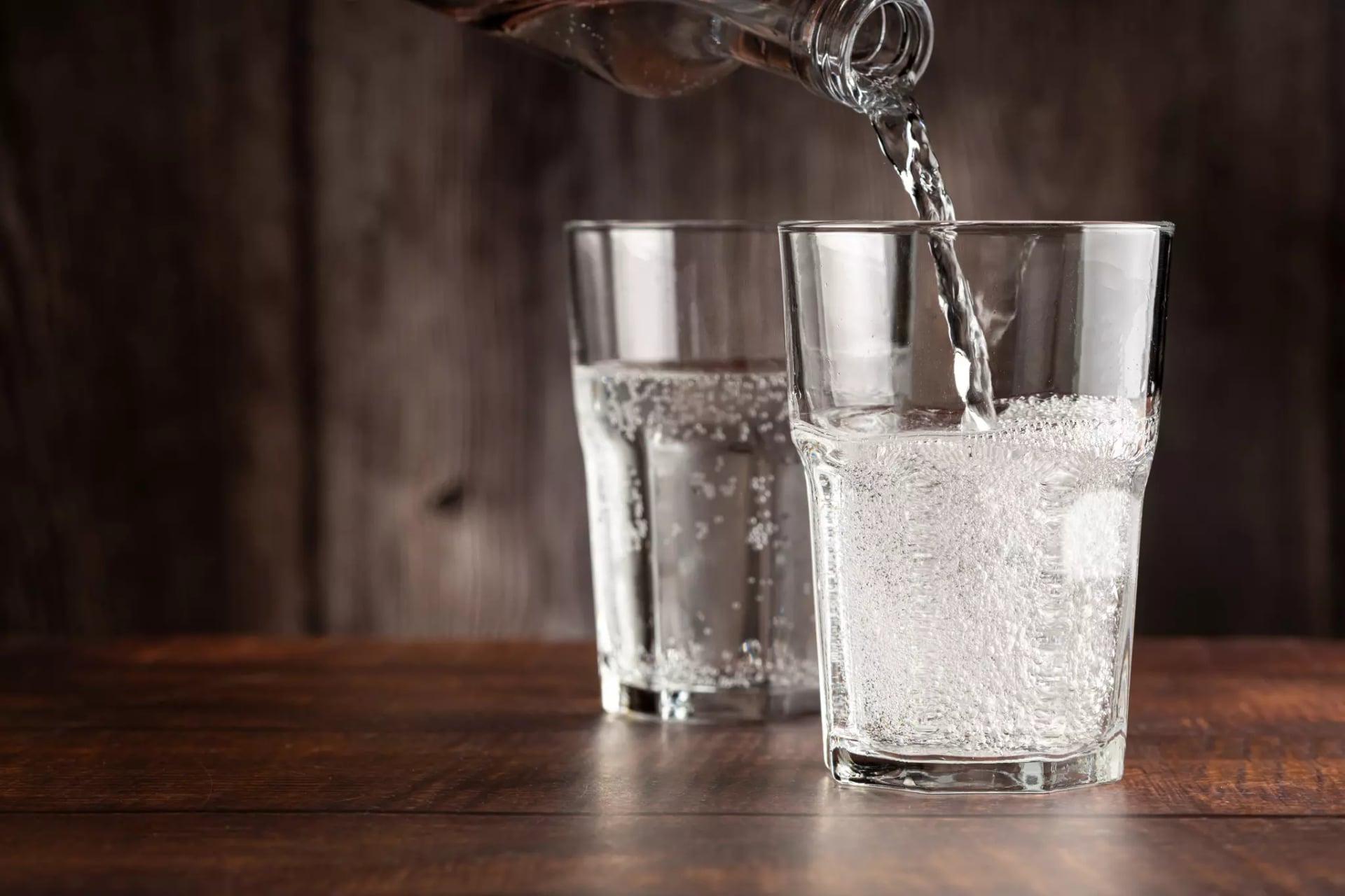 Zwei Gläser Wasser mit Sprudel, in das eine wird gerade noch aus einer Glasflasche eingegossen