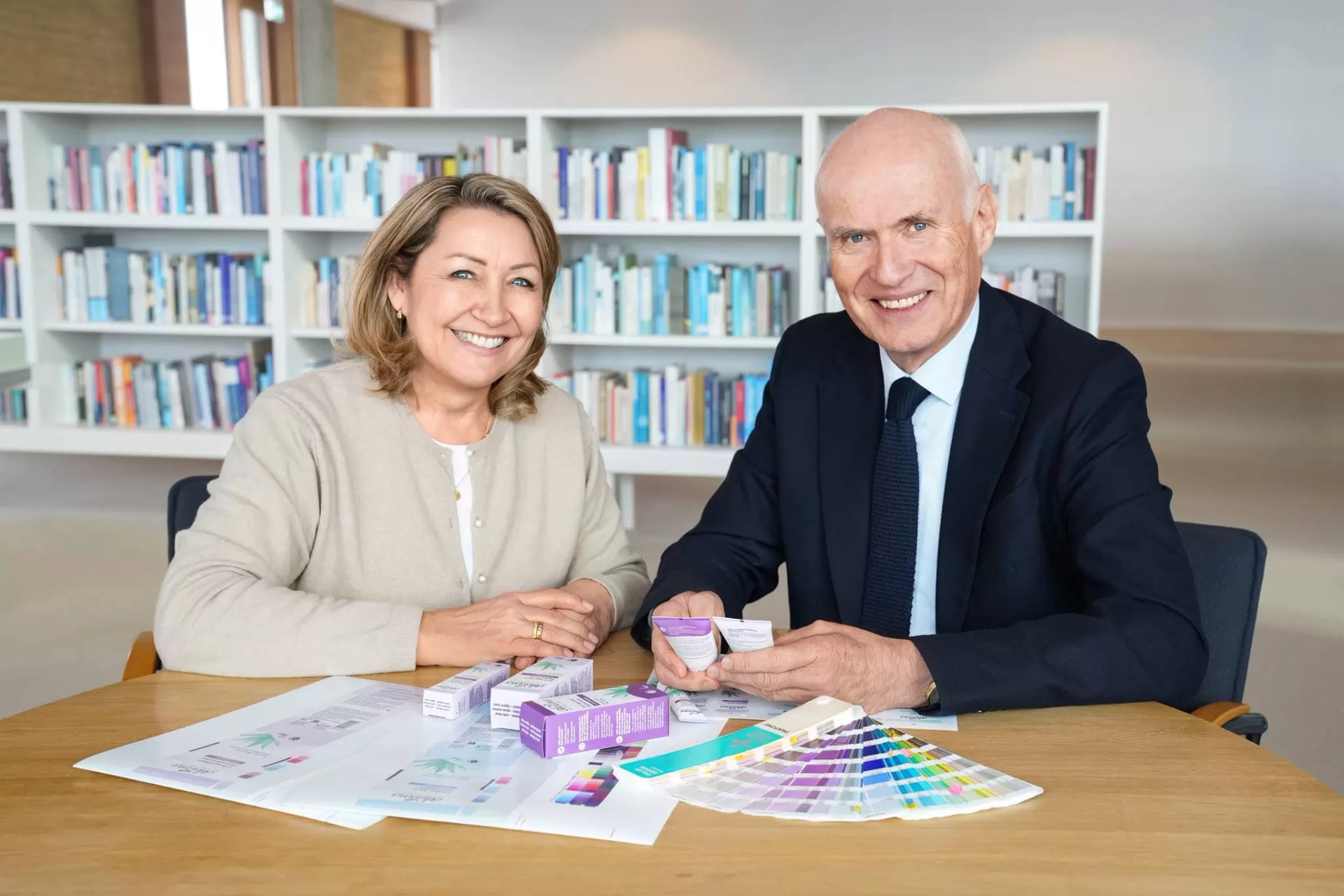 Alnatura Gründer Götz Rehn und alviana Teamleiterin Stefanie Müllers bei der Produktentwicklung. Vor ihnen auf dem Tisch liegen mehrere alviana Produkte Farbdrucke mit Produktentwürfen.