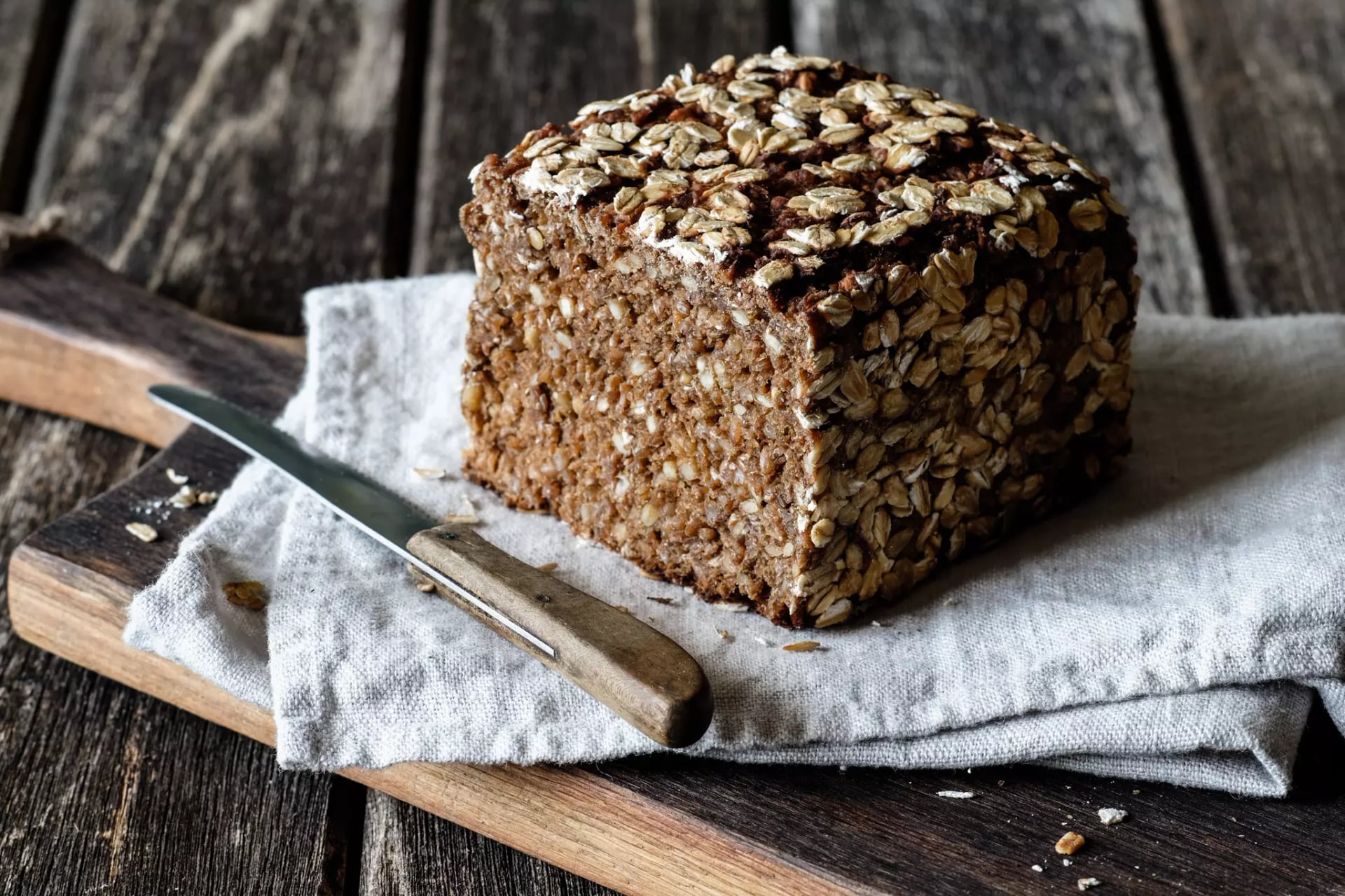 Ein angeschnittenes Roggenvollkornbrot auf einem hellgrauen Baumwolltuch welches widerrum auf einem Holzschneidebrett liegt