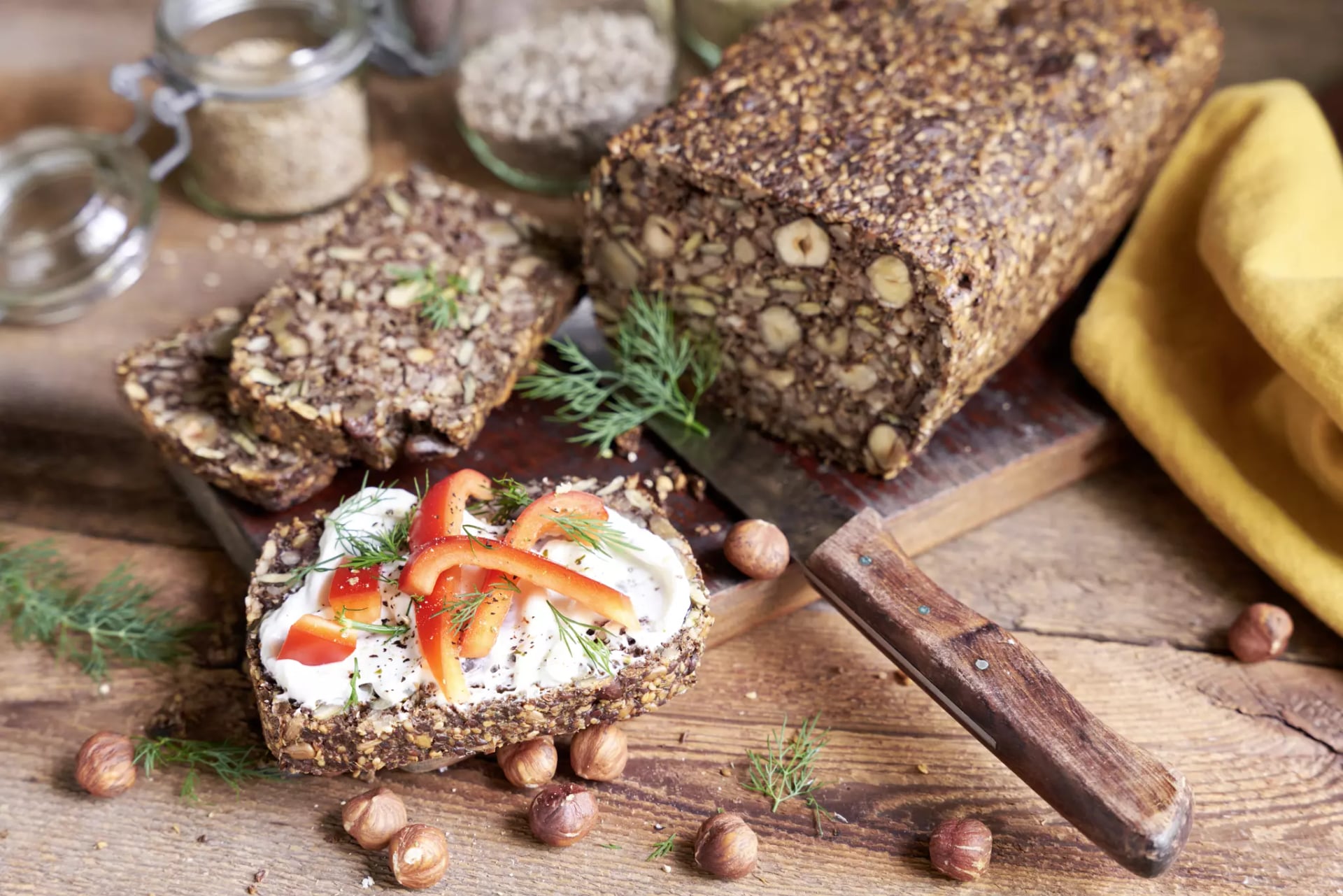 Brot ohne Mehl mit drei aufgeschnittenen Scheiben eine mit Frischkäse und Paprikastreifen belegt.