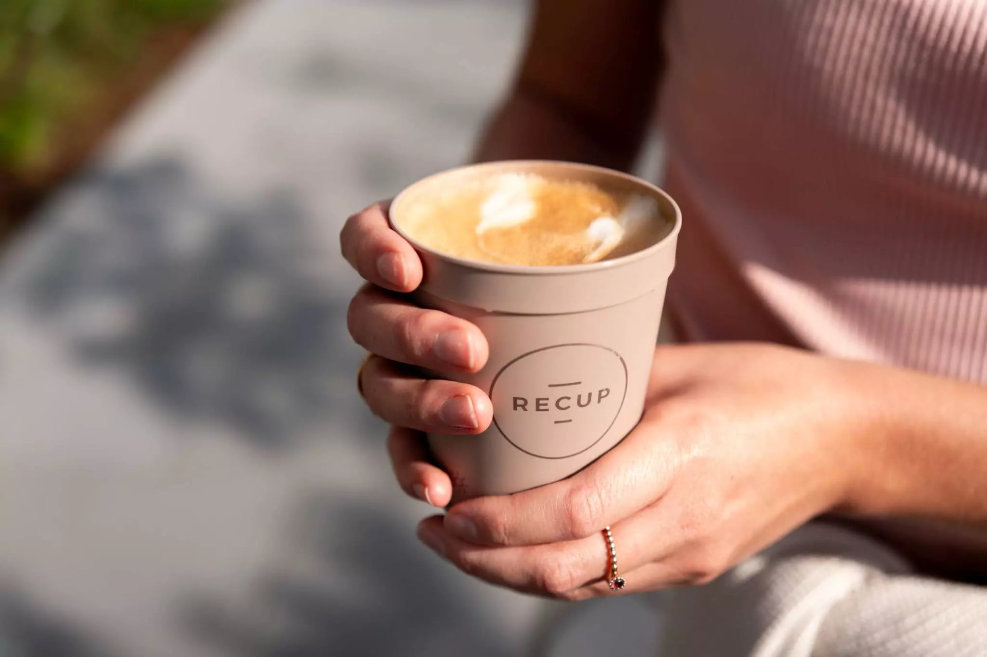 Ein beige farbener Recup gefüllt mit Kaffee wird von zwei Händen gehalten