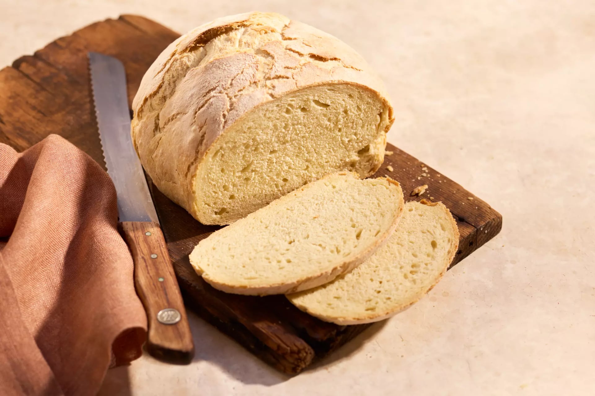 Angeschnittenes einfaches Rührbrot mit zwei Brot Scheiben, einem Brotmesser und einem Tuch auf einem Holzbrett.