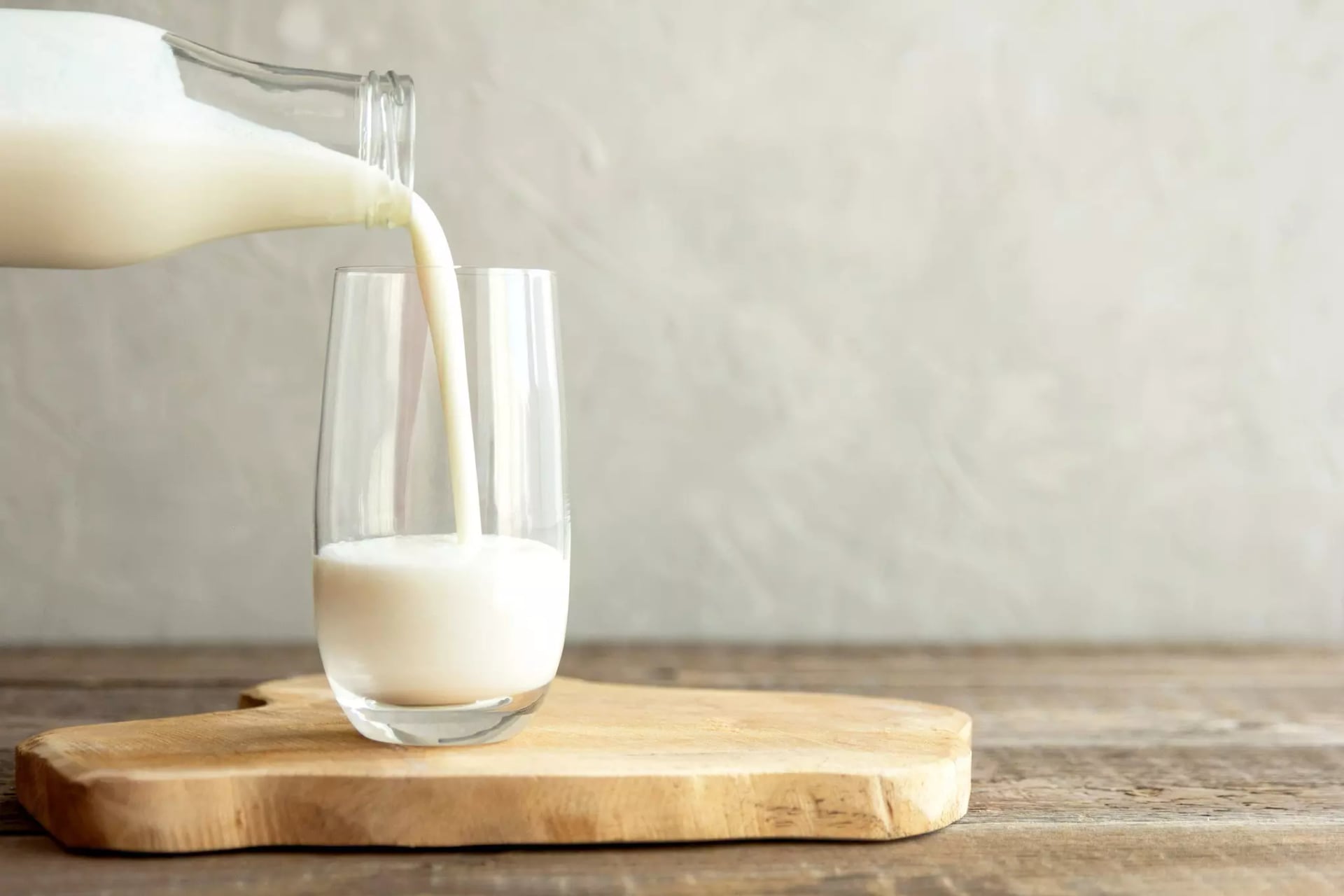 Ein Glas das auf einem Holzbrett steht wird gerade über eine Schraubglasflasche mit Milch gefüllt