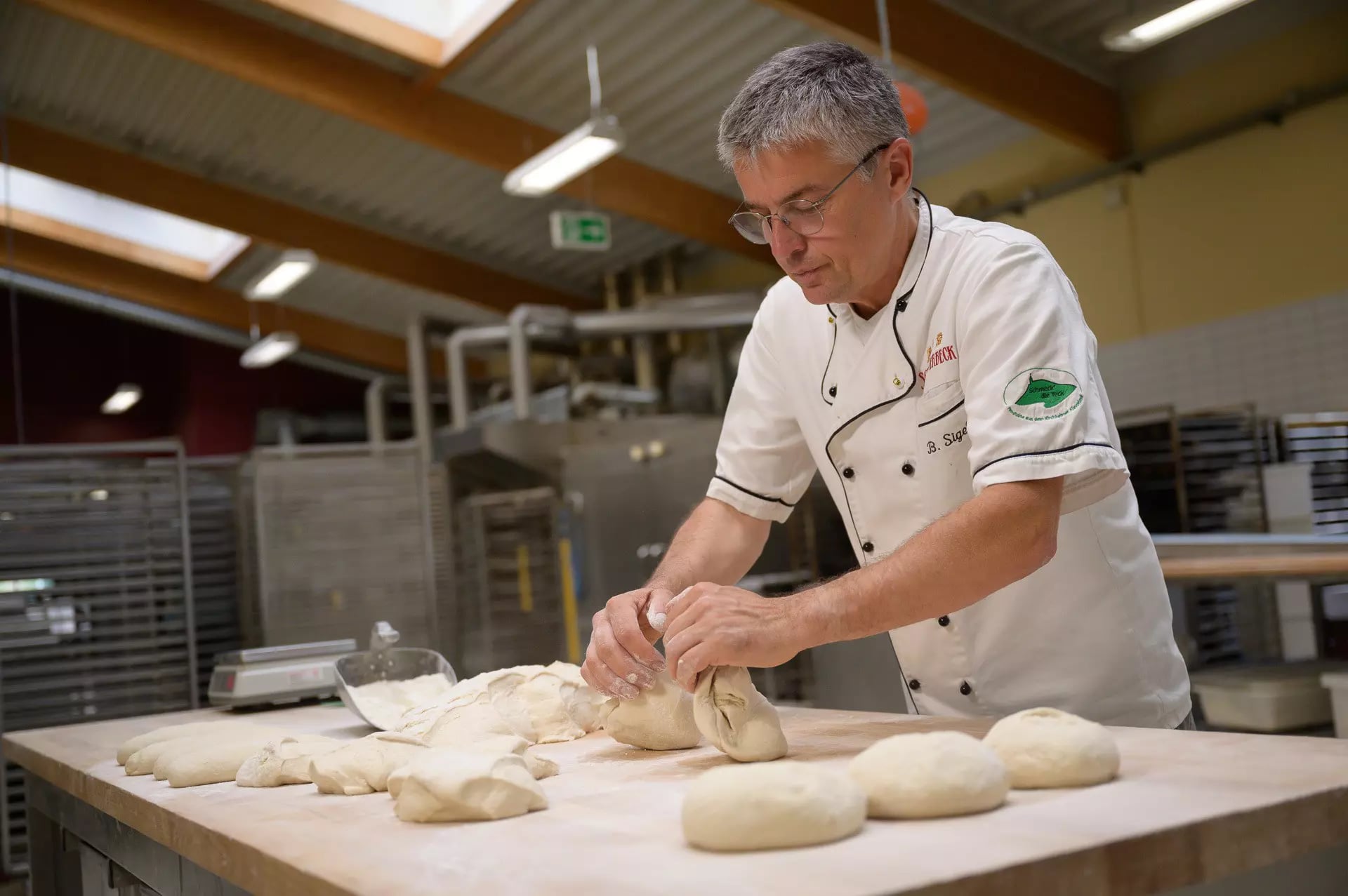 Ein Bäcker teilt Teig in gleich große Stücke um daraus kleiner runde Brotlaibe zu formen