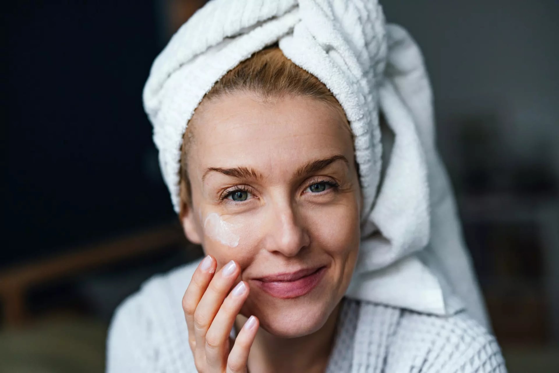 Eine blonde Frau trägt einen Handtuch-Turban und cremt sich im Gesicht ein