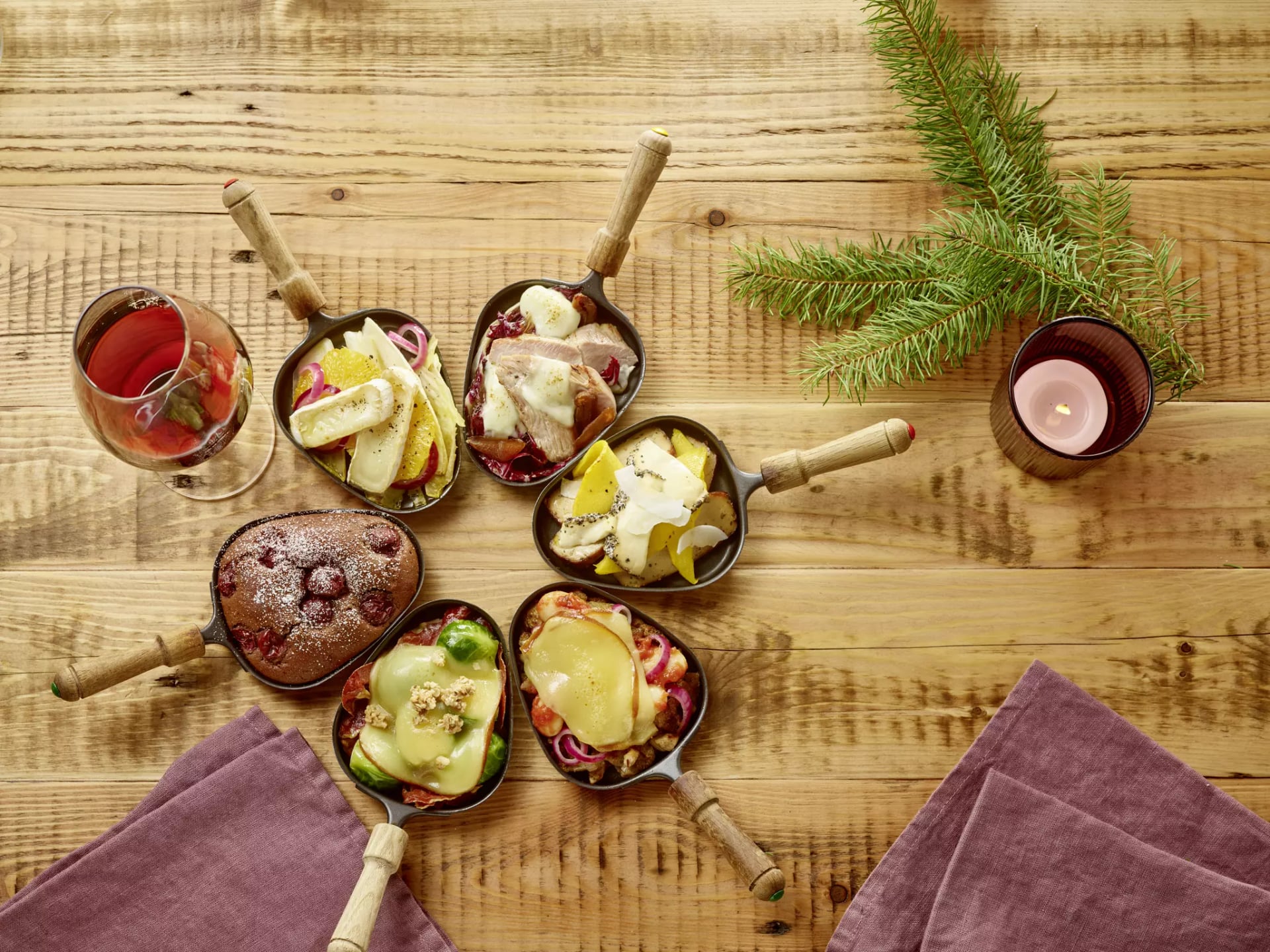 Raclette-Pfännchen mit unterschiedlichen Füllungen. Rosenkohl, geräucherter Käse, Zwiebeln, Camembert, Kirschen.