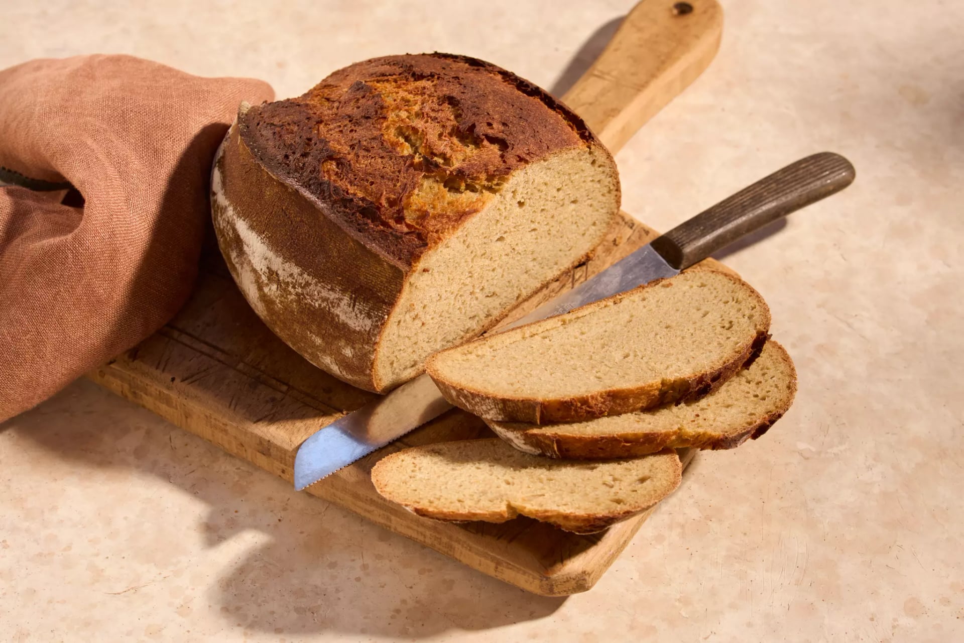 Angeschnittenes Kartoffelbrot mit mehreren Brotscheiben und einem Messer auf einem Holzbrett.