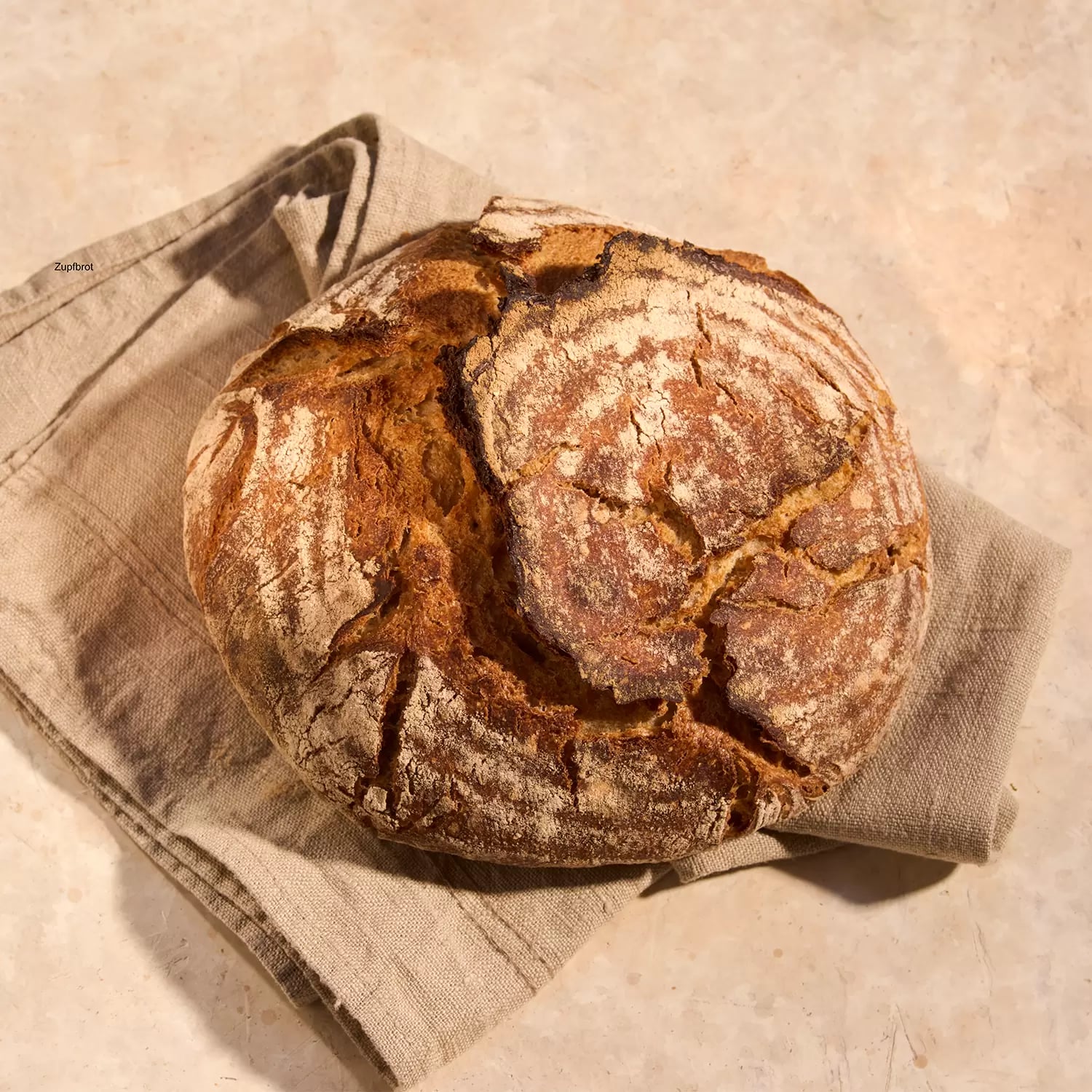 Ein Laib Sauerteigbrot liegt auf einem beige-farbenen Tuch