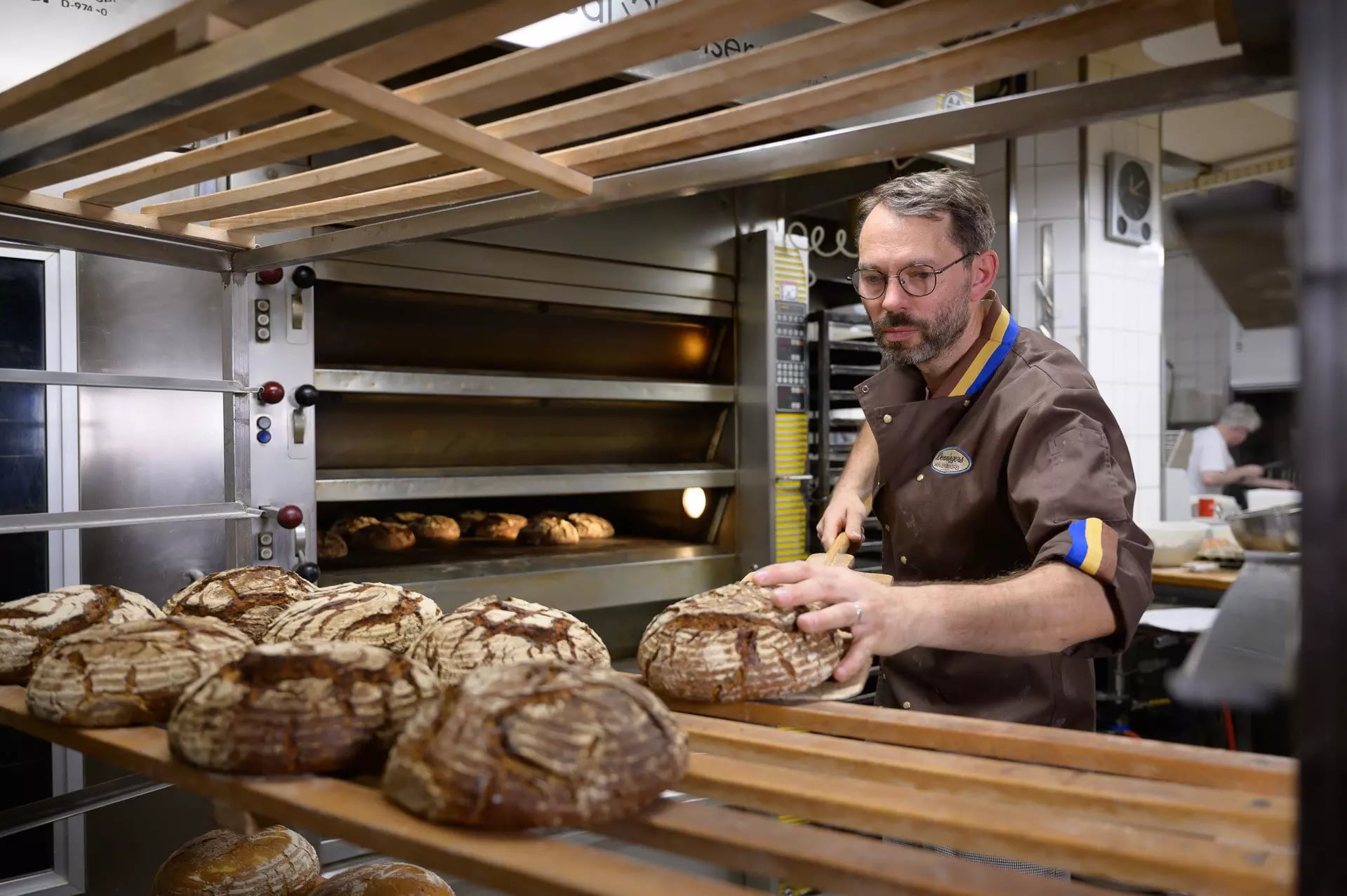 Ein Bäcker holt fertige, runde Brotlaibe aus dem Ofen