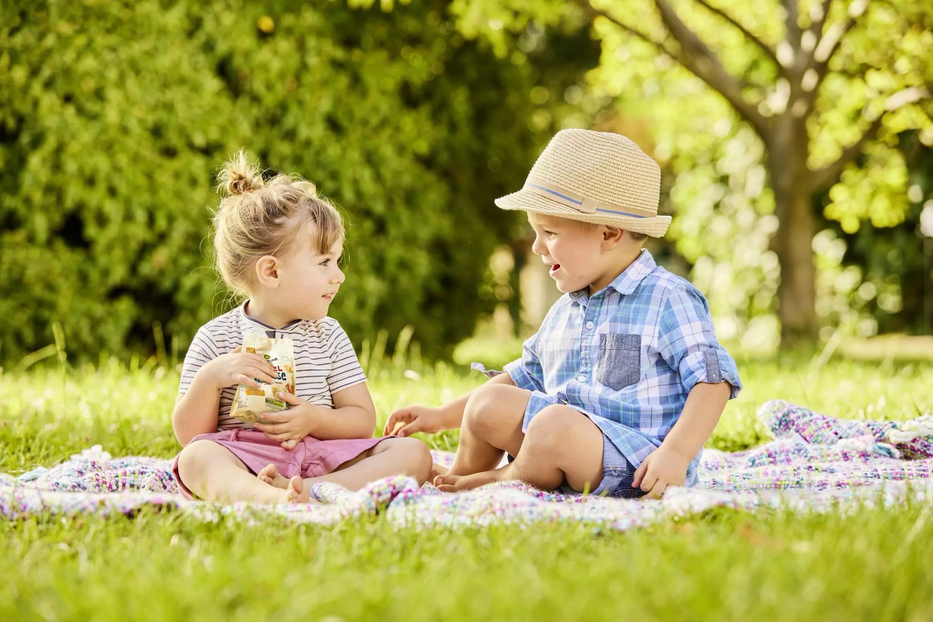 Zwei Kleinkinder sitzen auf der Wiese und naschen Kekse.