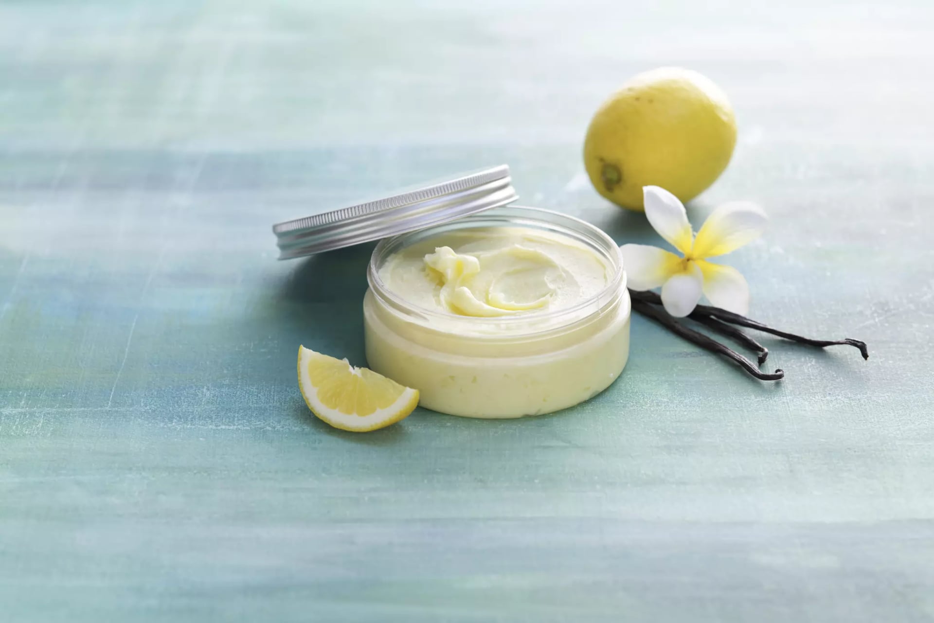 Geöffnete Dose mit Körperbutter, daneben drei Vanilleschoten und Zitrone.