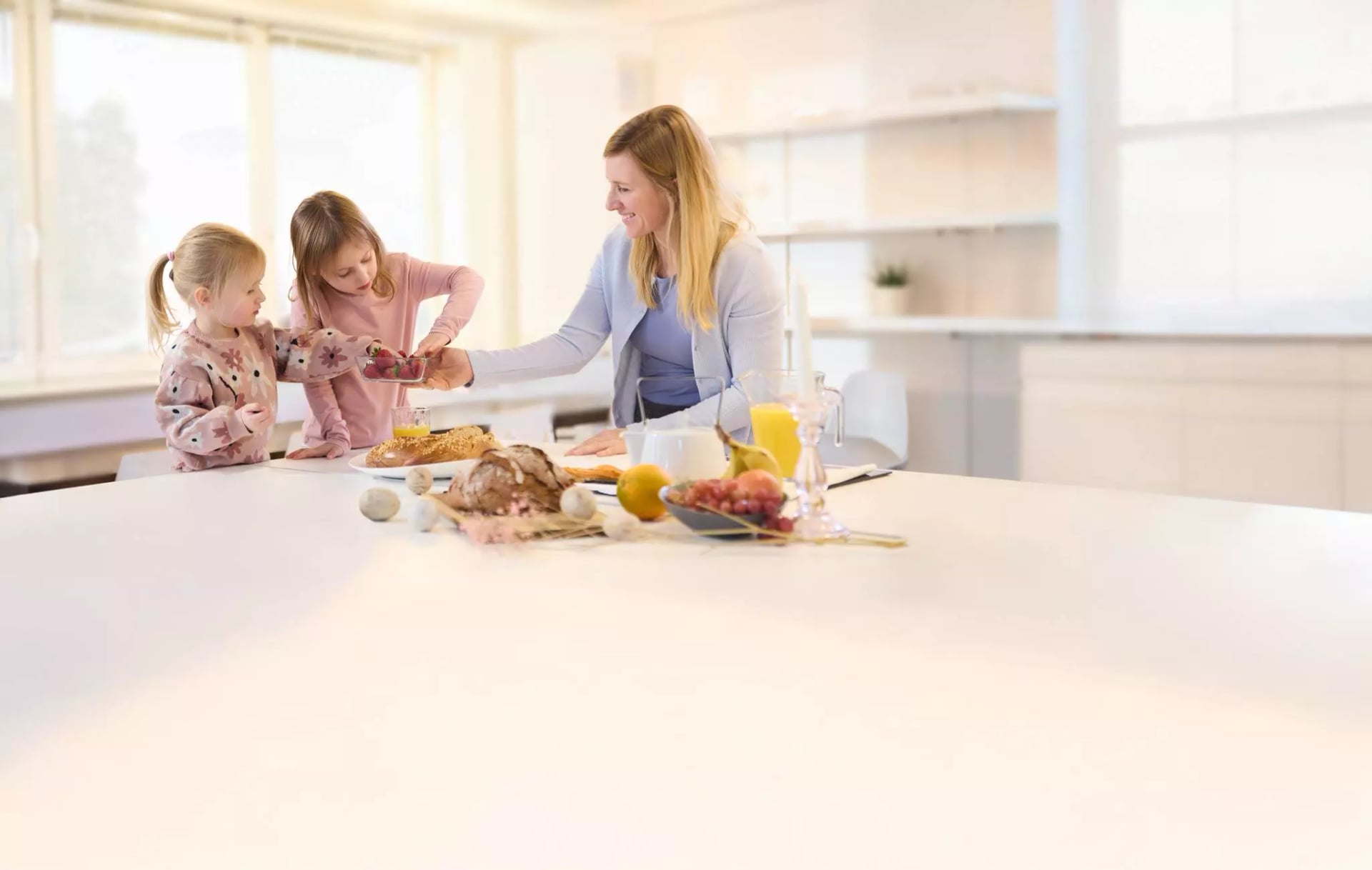 Frau mit zwei Kindern beim Essen von Erdbeeren.