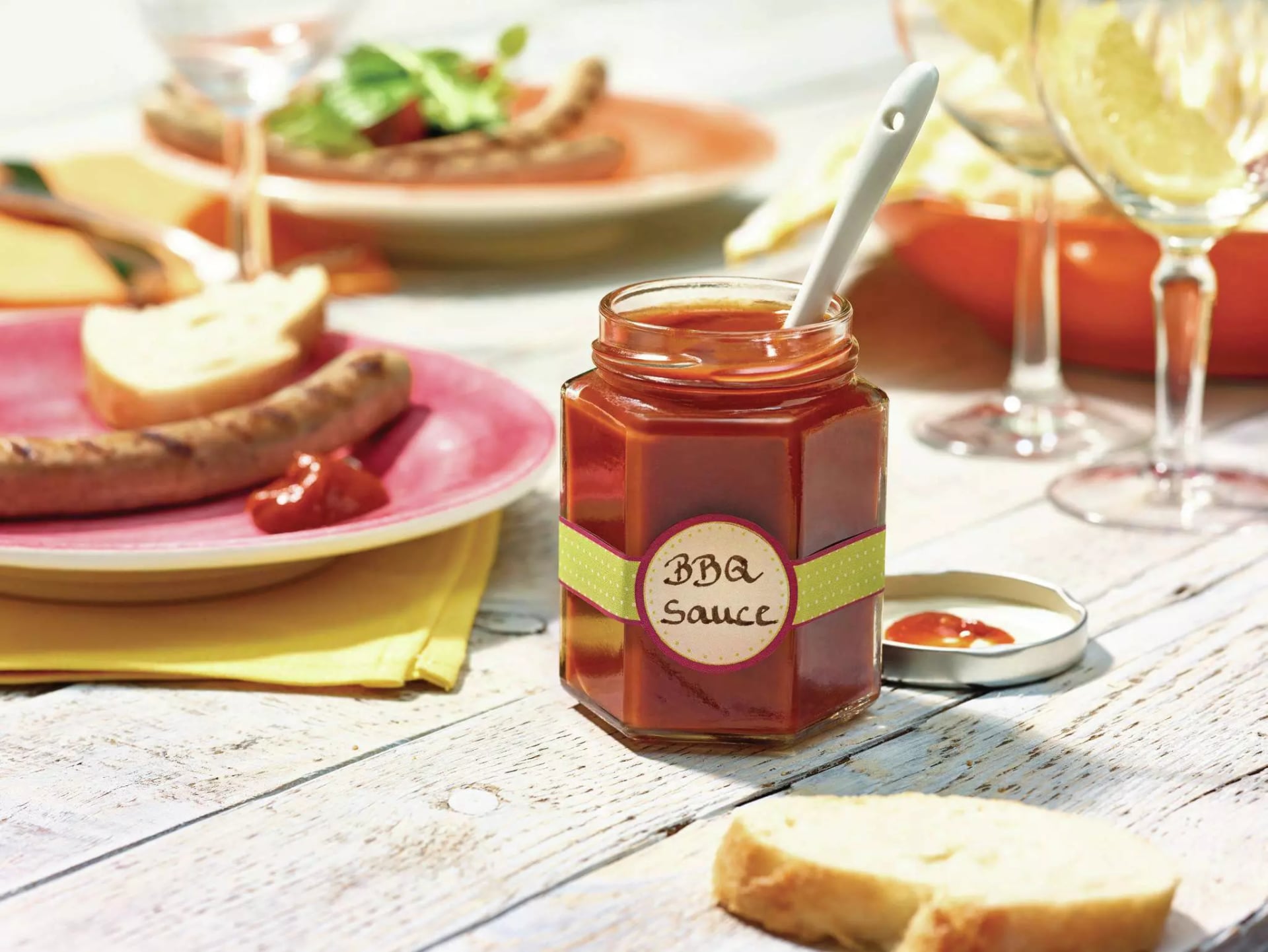 Eine selbst gemachte Barbecue-Sauce in einem Glas steht auf einem Holztisch. Im Glas steckt ein Löffel und das Glas ist mit "BBQ Sauce" beschriftet.