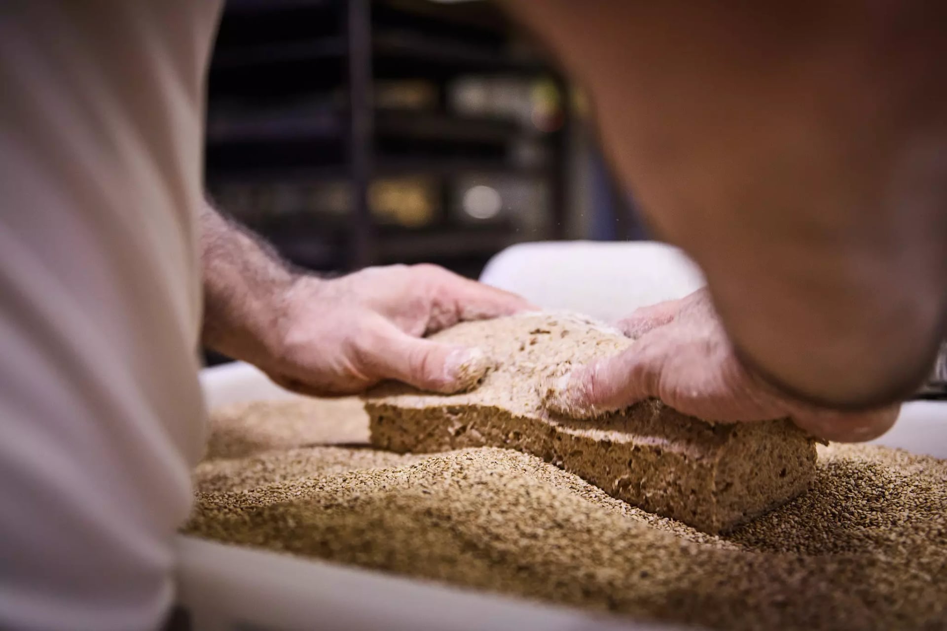 Zwei Hände, die ein Brot in Samen wälzen