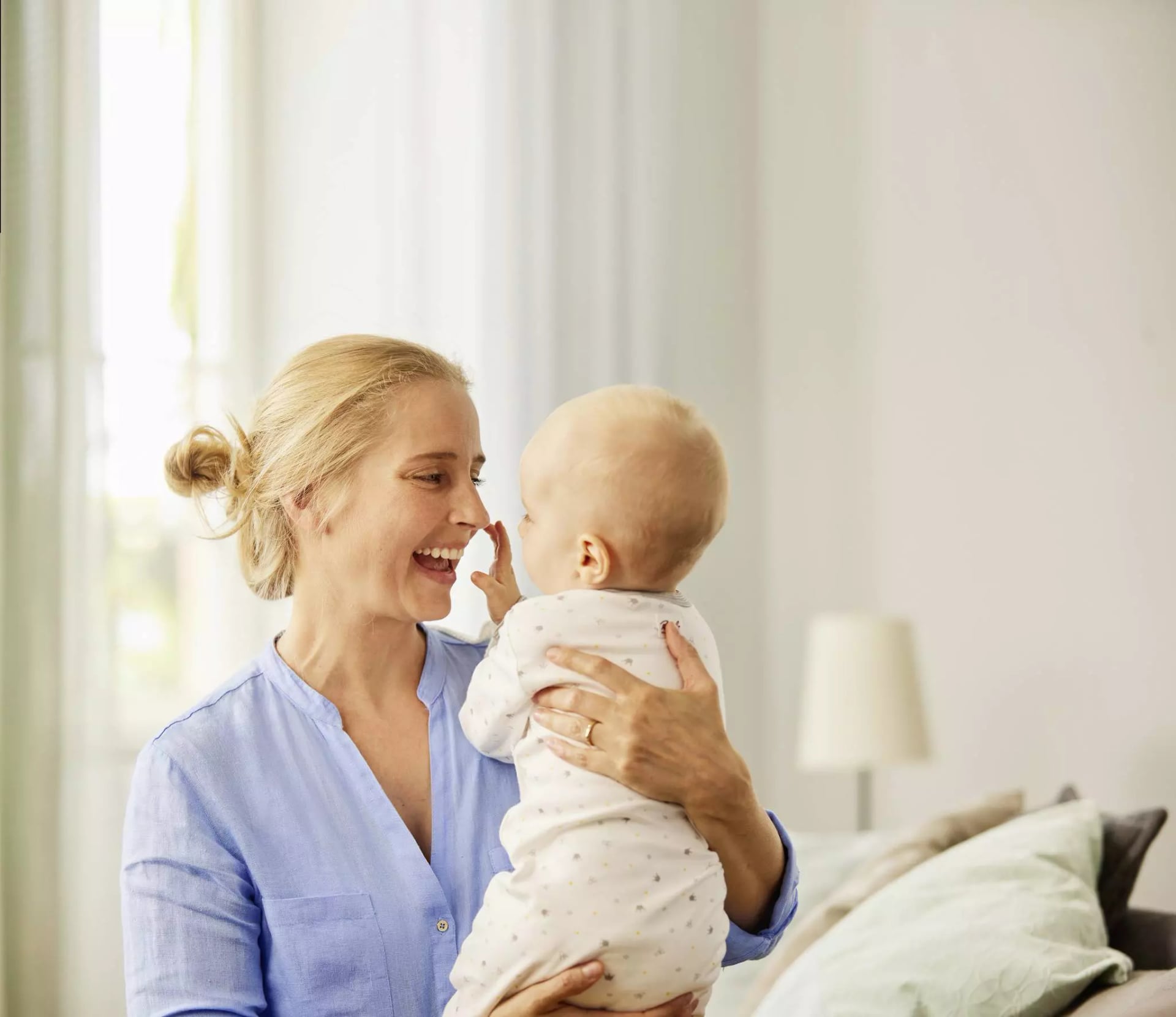 Mutter hält ihr Baby im Arm und lacht es an.