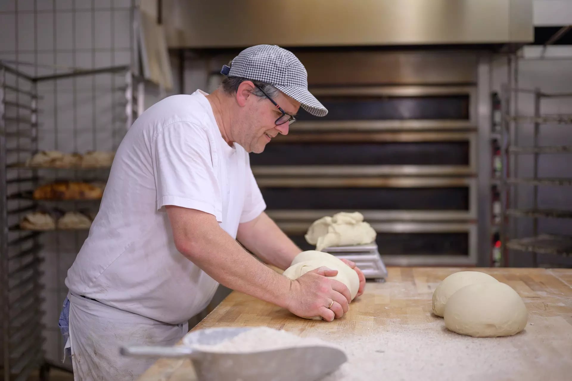 Ein Bäcker kneten zwei Laibe Brot auf einer bemehlten Arbeitsfläche