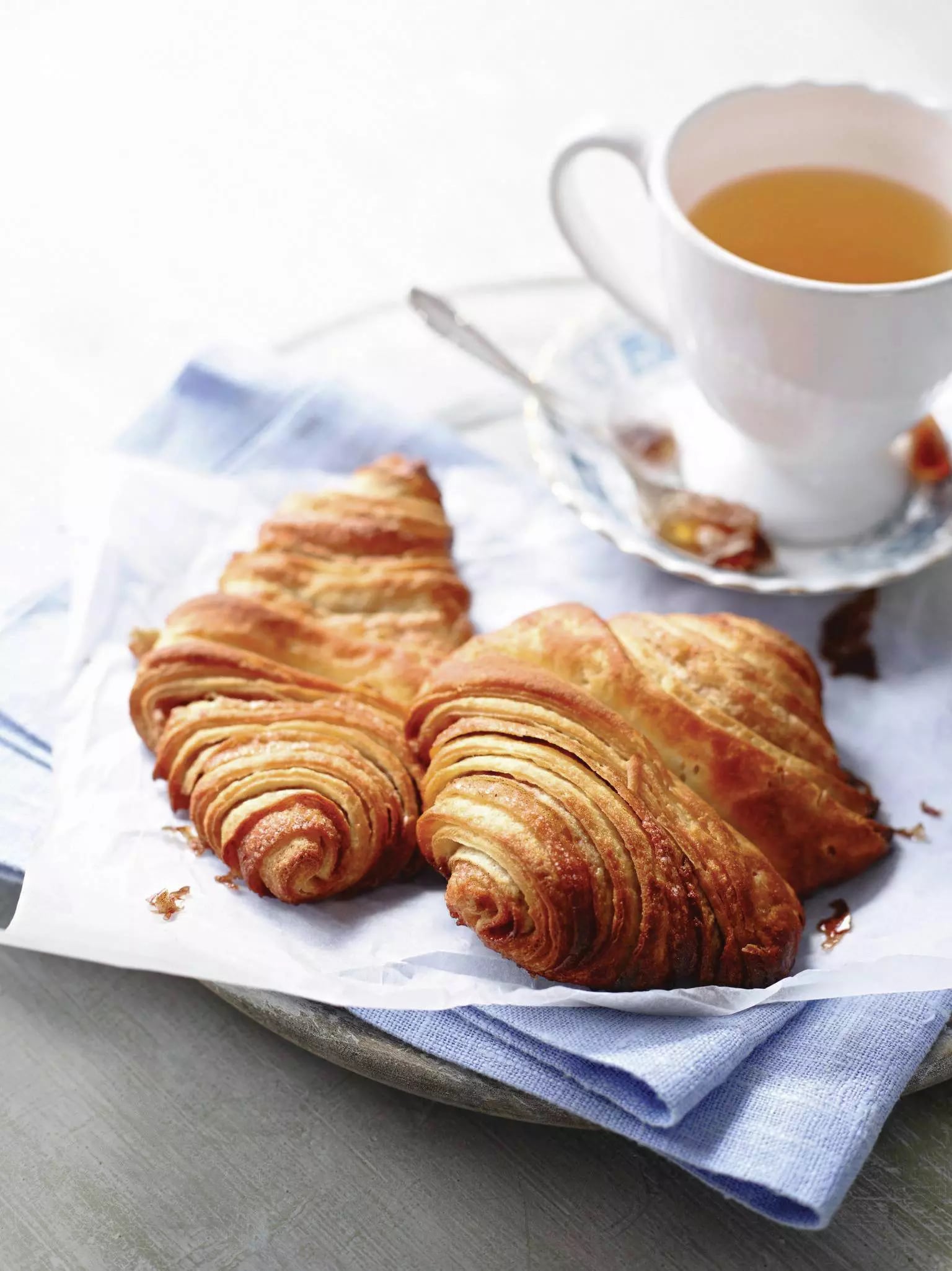 Zwei Franzbrötchen neben einer mit Tee gefüllten Tasse.