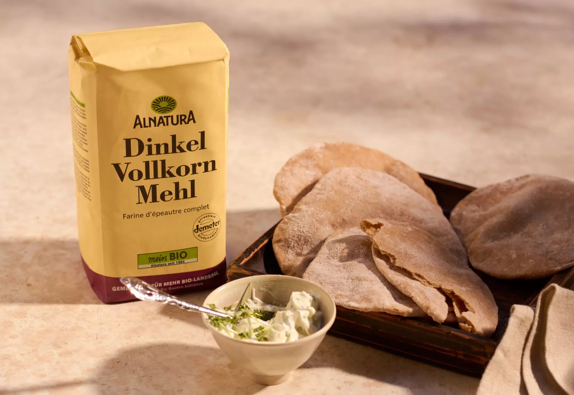 Eine Packung Dinkelvollkornmehl neben mehreren Drei-Zutaten-Fladenbroten und einer kleinen Schale mit Dip.
