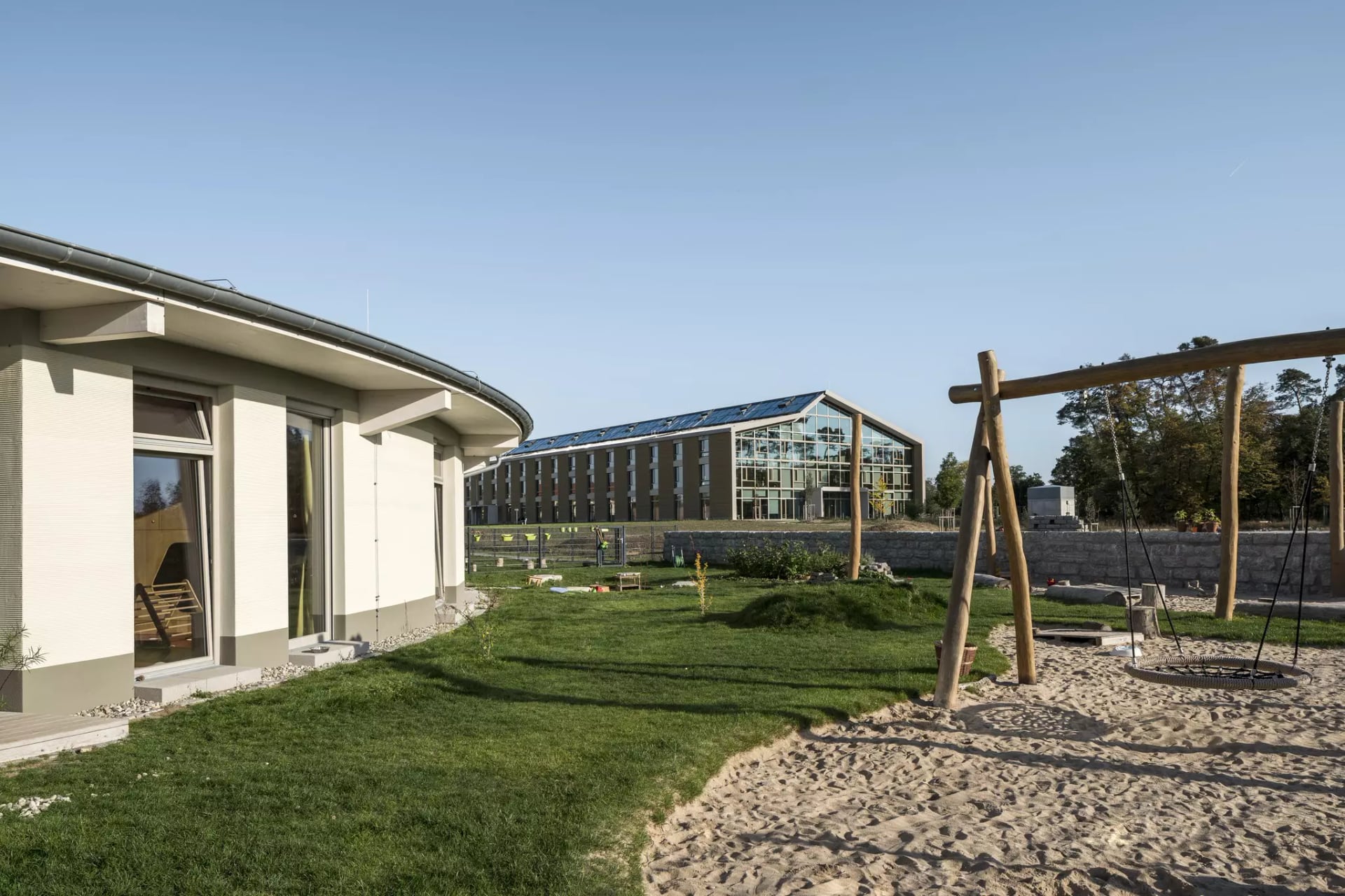 KinderNaturGarten im Hintergrund  Campusgebäude. Rechts eine Nestschaukel.