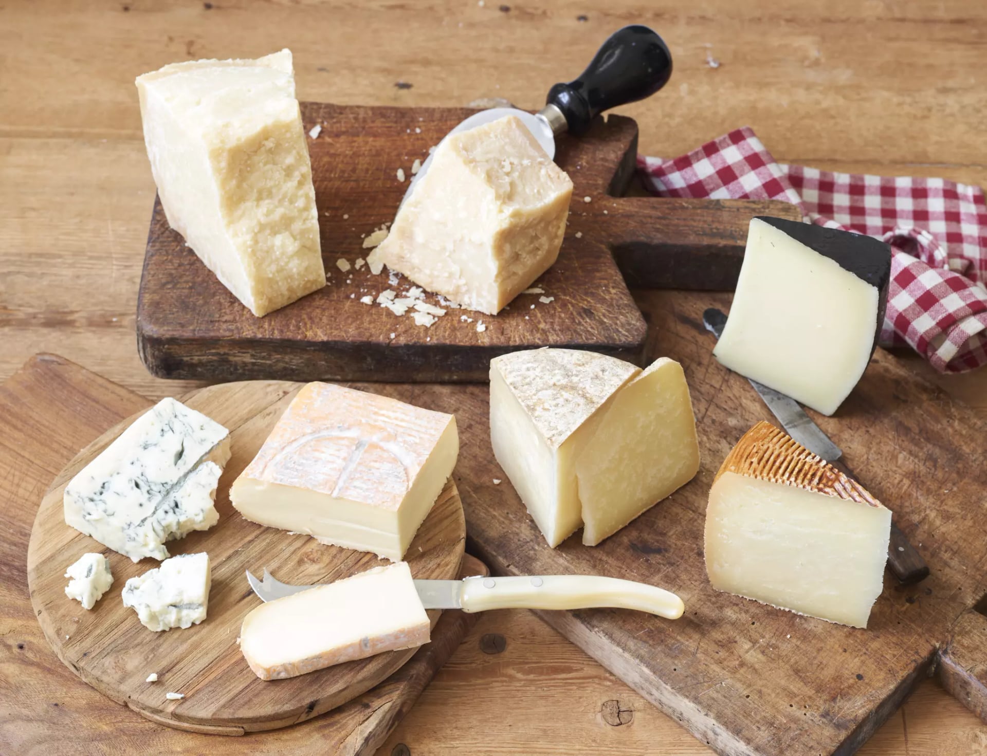 Warenkunde Käse, sieben verschiedene Käsesorten auf Holzbrettern mit Käsemessern.