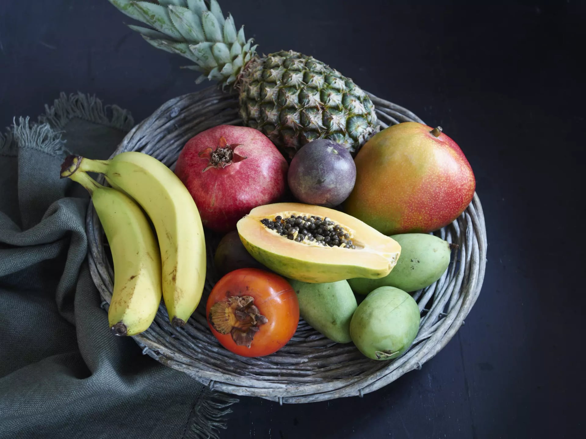 Verschiedene Exotische Früchte, Mango, halbe Papaya, Granatapfel, Banane, Maracuja, Ananas und Kaki in einem Korb.