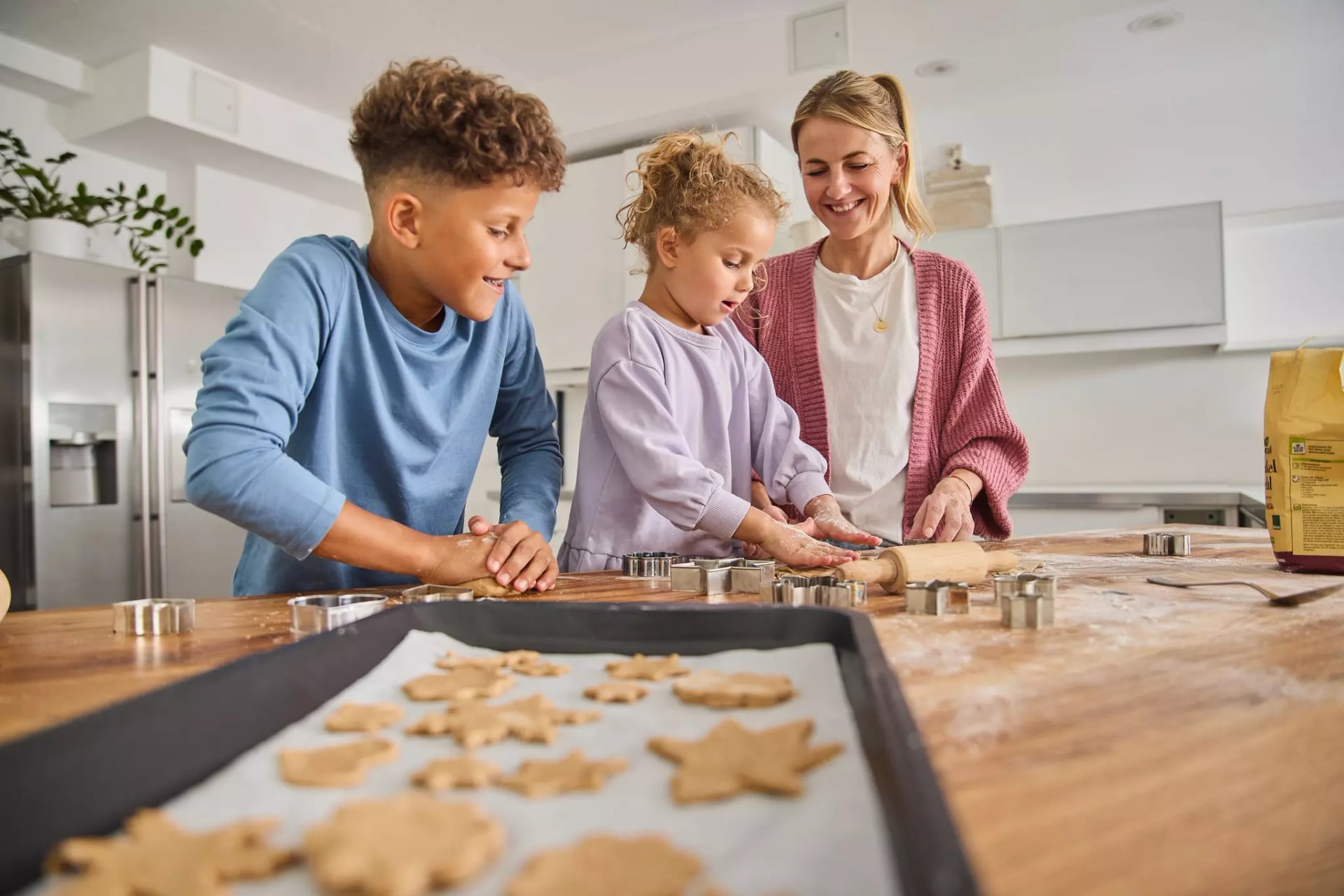 Zwei Kinder und eine Frau beim Plätzchen backen. Stechen mit Förmchen Plätzchen aus.