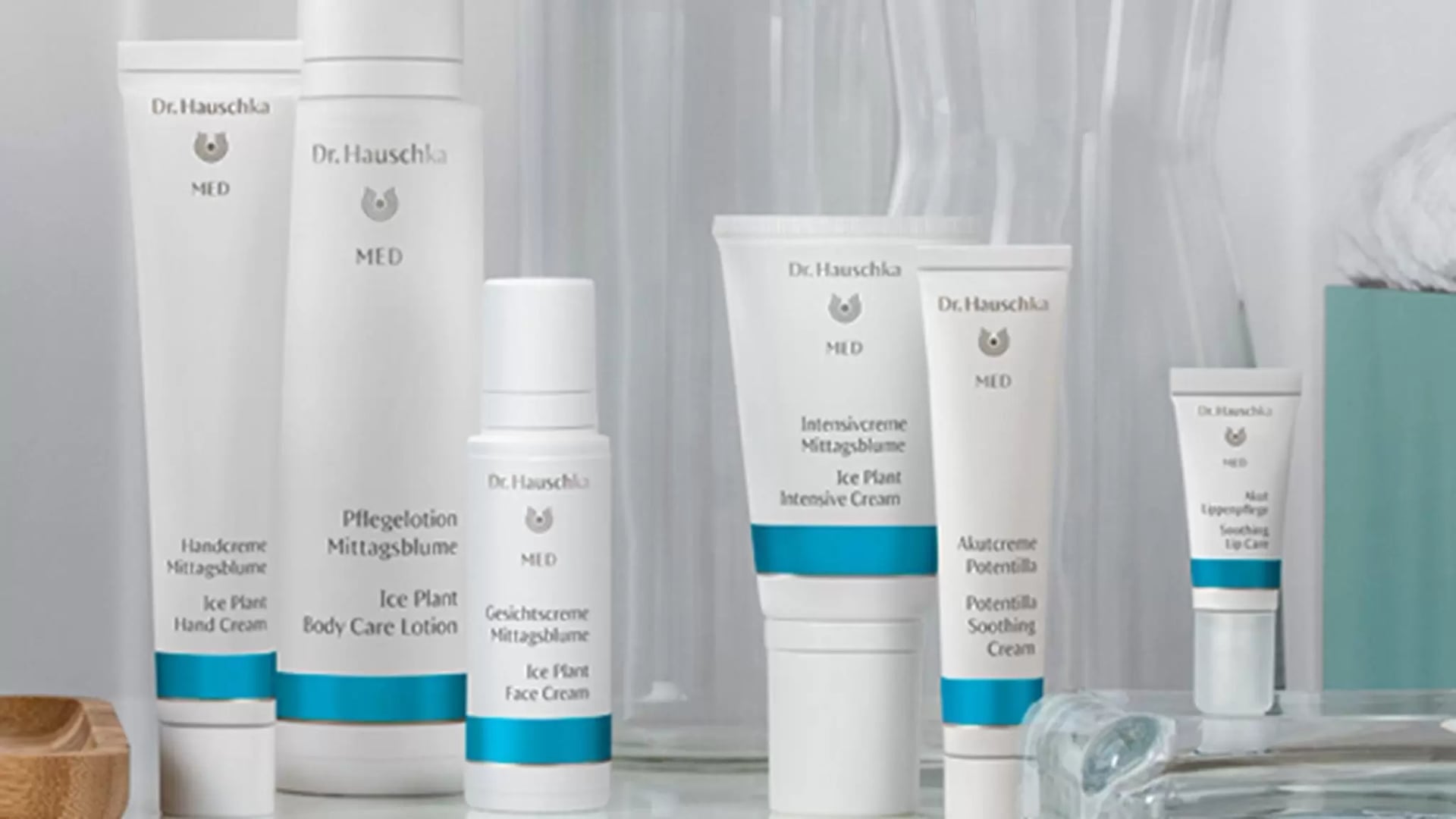 Mehrere Dr. Hauschka weiße Tuben und Flaschen mit blauen Akzenten der Dr. Hauschka MED Hautpflegeprodukte auf einem weißen Untergrund.