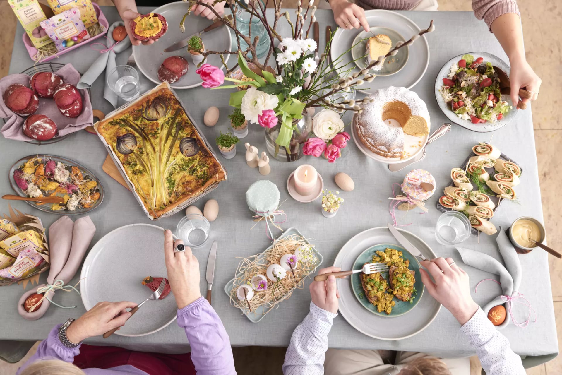 Ostertafel mit verschiedenen Speisen, Blumenstrauß und vier Personen, die von oben zu sehen sind