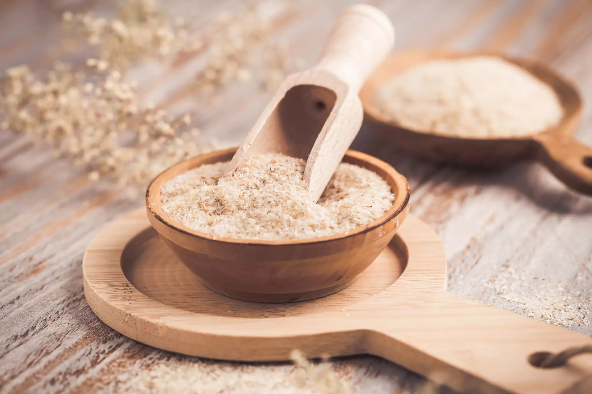 Flohsamenschalen in einer Holzschüssel mit Holzlöffel auf einem Holzbrett.