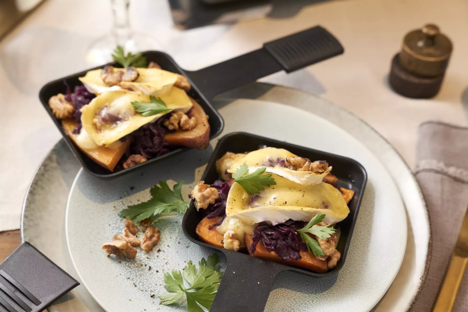Zwei kleine schwarze Pfannen mit Toast, Walnüssen, Käse, roten Zwiebeln und Petersilienblättern auf einem grauen Teller.