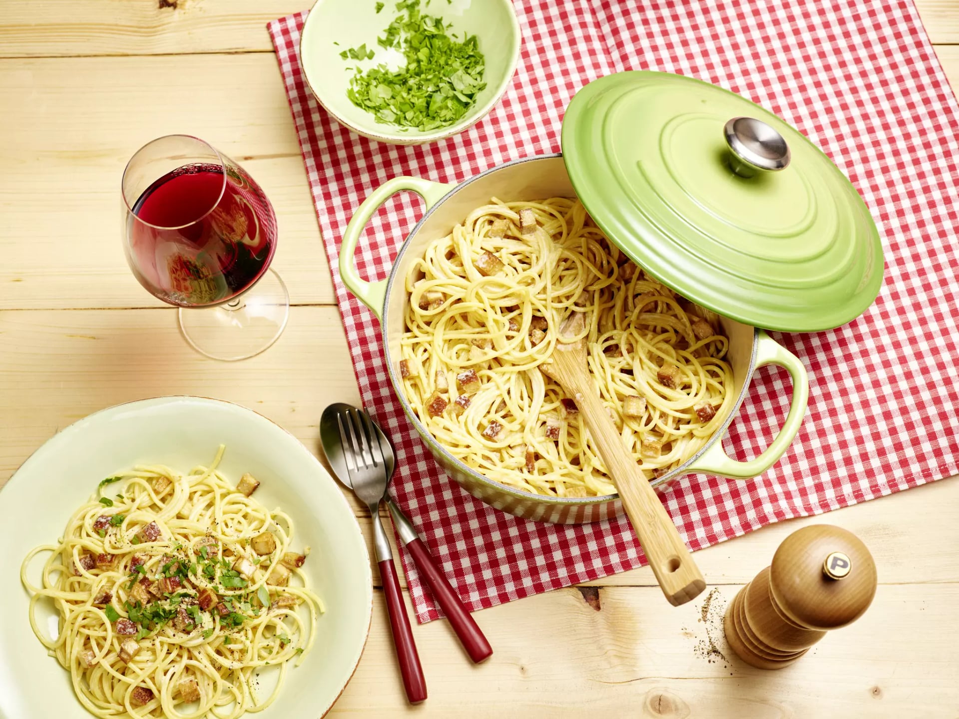 Topf mit Spaghetti Carbonara, davor Teller mit Carbonara, Besteck und Weinglas.