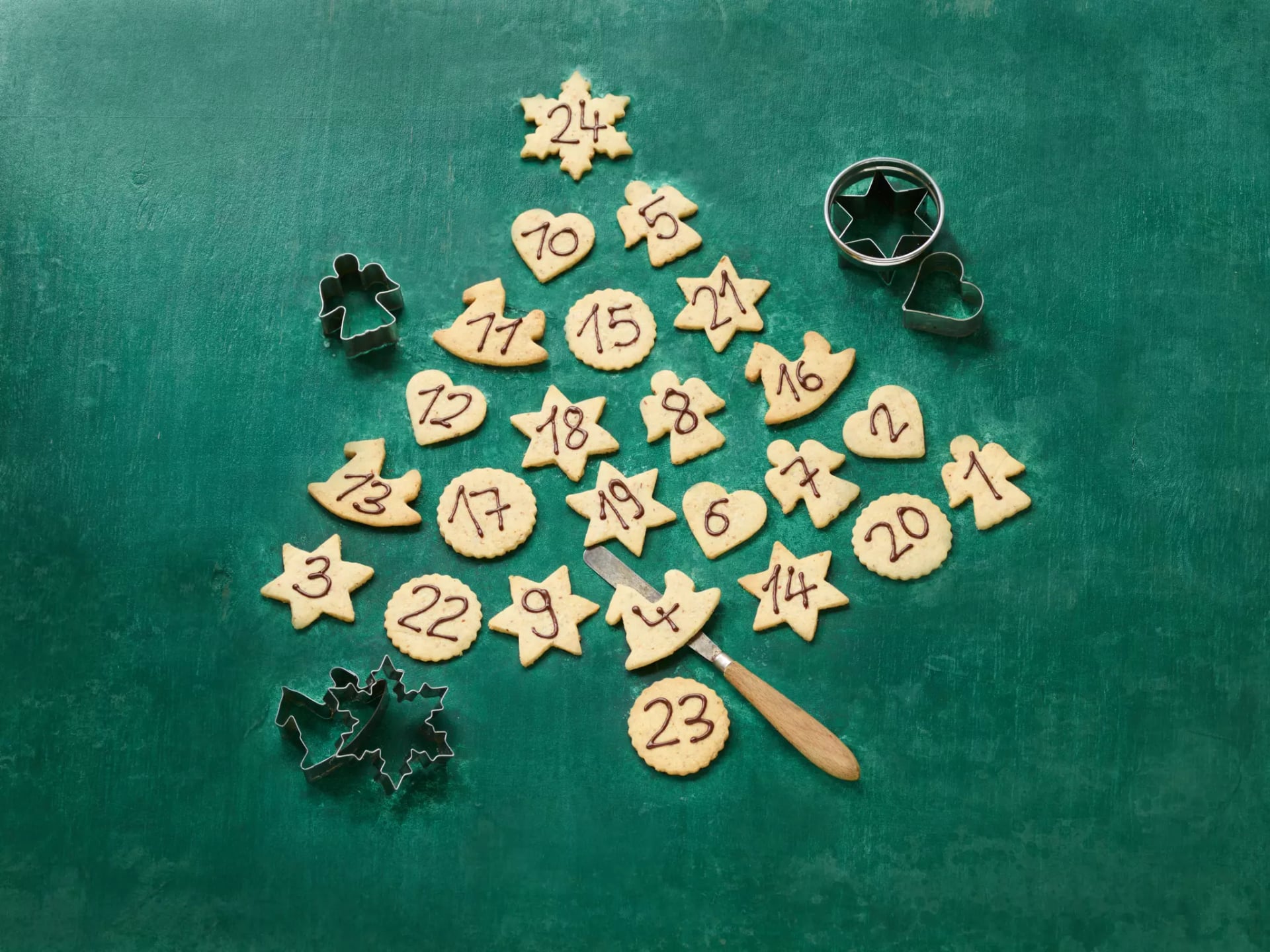 Butterplätzchen mit Adventskalenden Nummerierung liegen in Form eines Tannenbaumes auf grünen Untergrund.