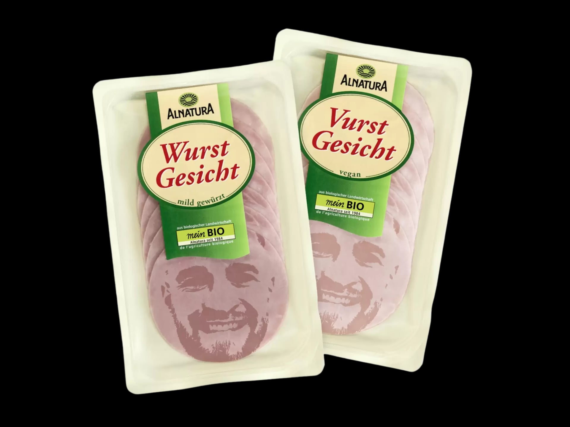 Zwei Packungen Alnatura Wurst Gesichtsaufschnitt mit Gesichtsmotiven auf den Scheiben, eine mild gewürzt, die andere vegan