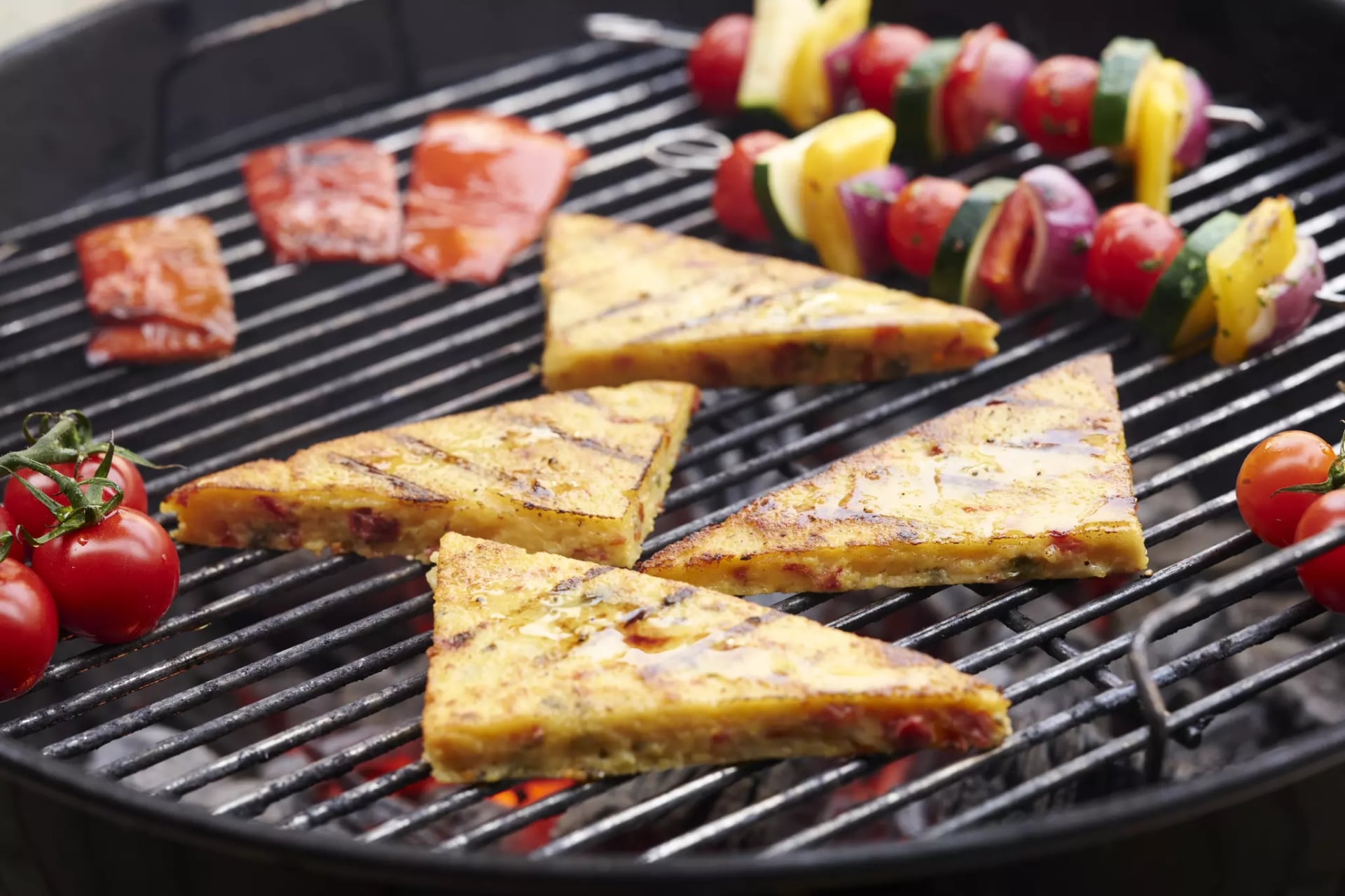 Dreieckige Tortilla-Stücke und Gemüsespieße mit Tomaten auf einem Grillrost