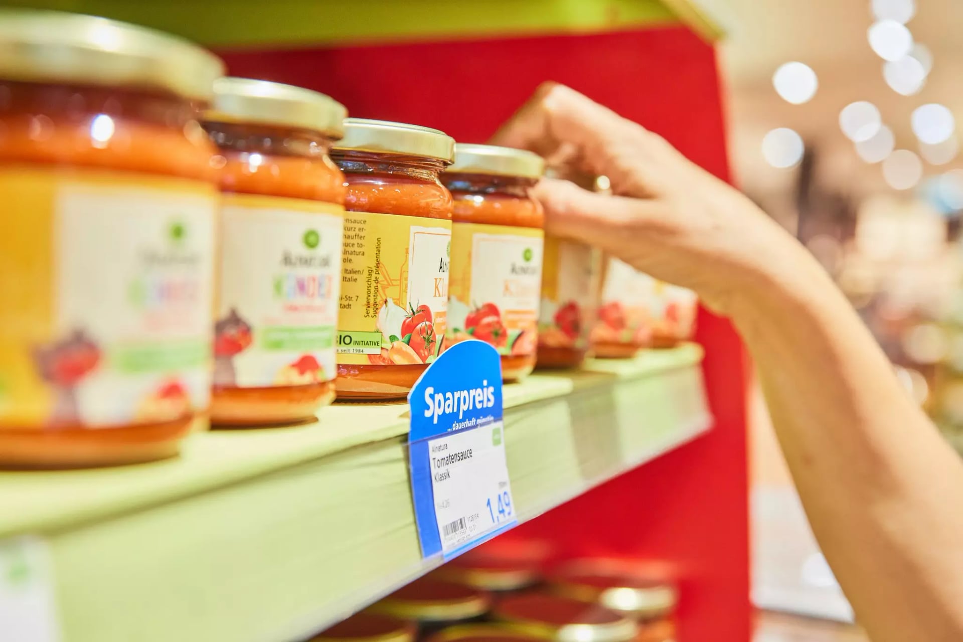 Eine Person greift eine Alnatura Tomatensauce aus einem Regal in einem Alnatura Markt.
