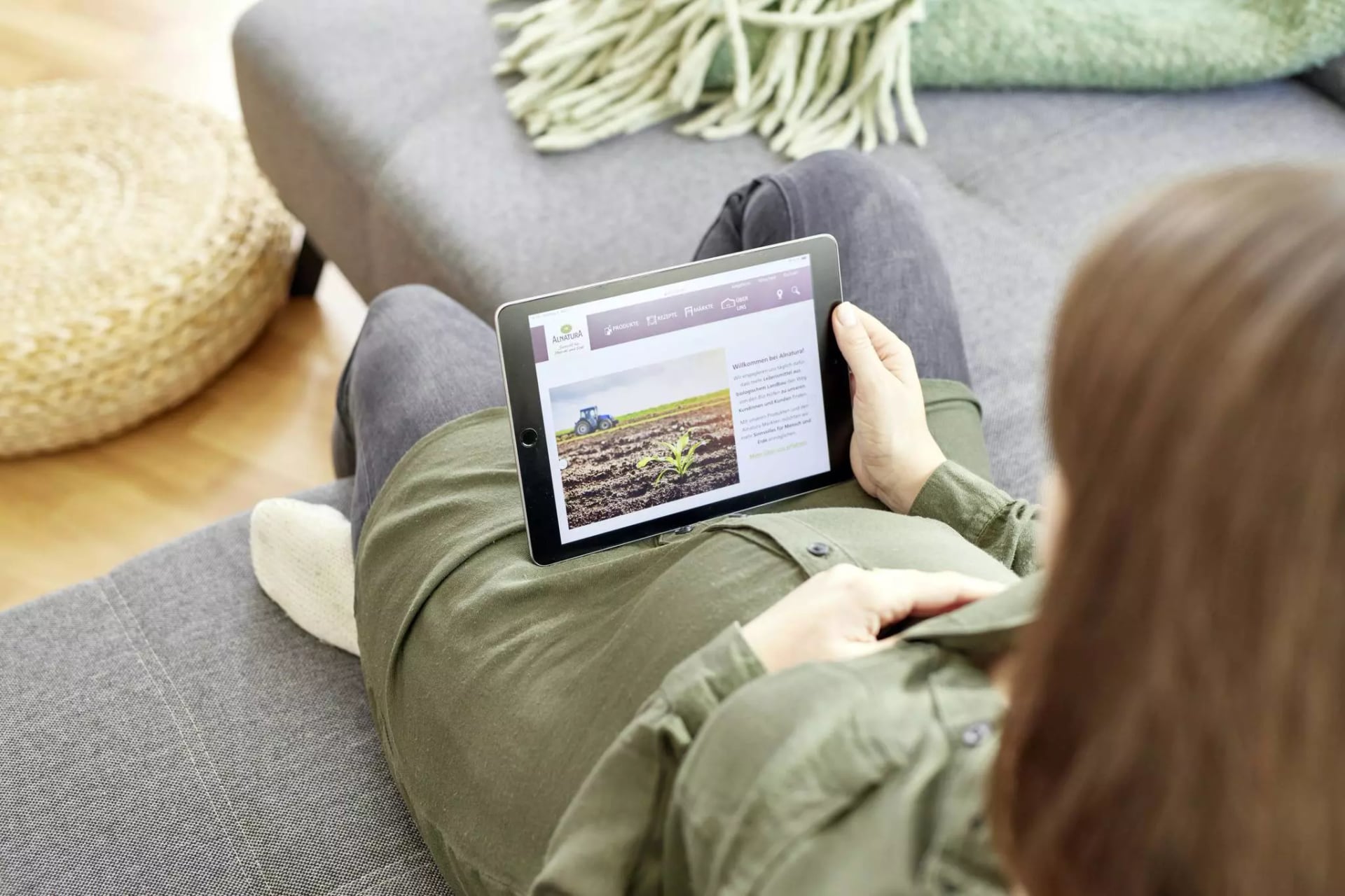Schwangere Frau mit einem Tablet auf dem Sofa. Auf dem Tablet ist die Alnatura Website geöffnet.