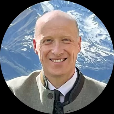 Porträt eines lächelnden Mannes mit Anzug vor Bergkulisse