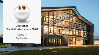Der Alnatura Campus in Darmstadt ist zu sehen. Er ist von innen beleuchtet, da es bereits dÃ¤mmert. Links auf dem Bild ist das Logo des "Deutscher Nachhaltigkeitspreis 2020" abgebildet mit dem Zusatz "Sieger Architektur"